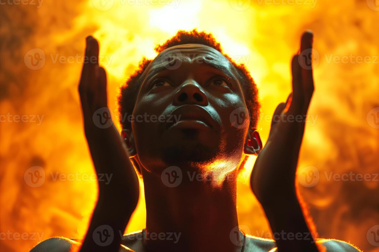 A male African descent with a powerful expression, hands raised towards an orange and yellow glowing backdrop, symbolizing hope and aspiration. photo
