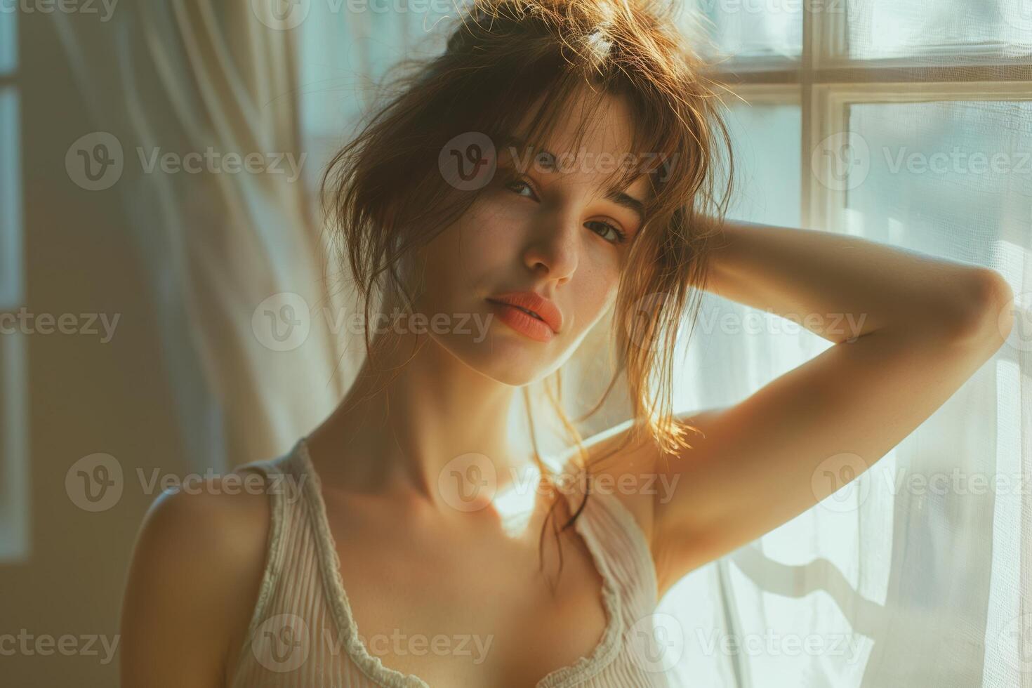 A young Caucasian woman with soft features poses naturally near a sunlit window. photo