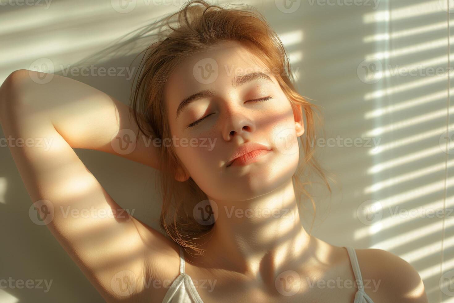 A serene young Caucasian woman relaxing with her eyes closed, bathed in soft sunlight and shadow patterns. photo