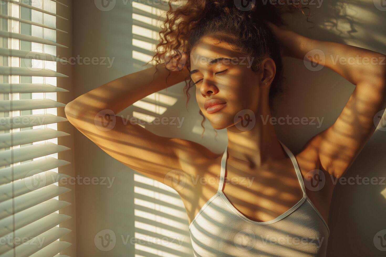 A young mixed-race woman poses gracefully with her eyes closed, sunlight casting playful shadows on her face. photo
