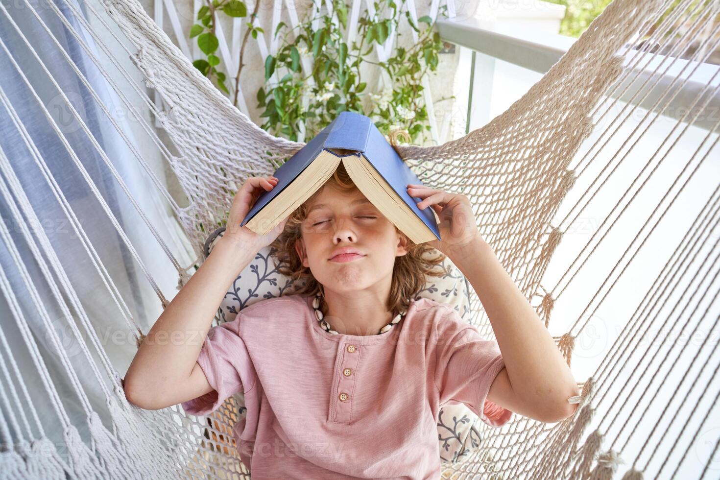 Boy with book on head lying in hammock photo