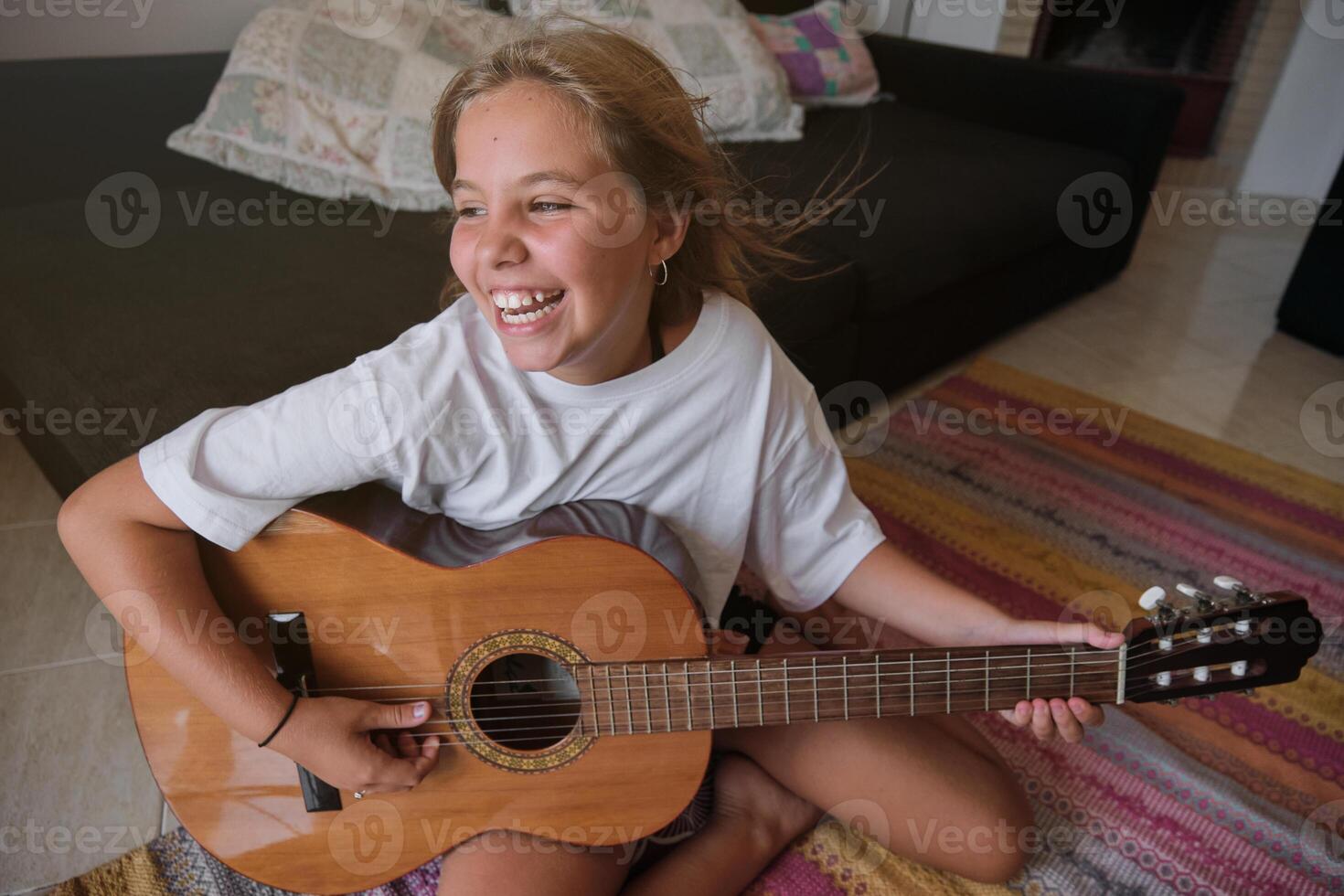 Girl sitting on the floor of a house playing a guitar and singing with happy expression photo