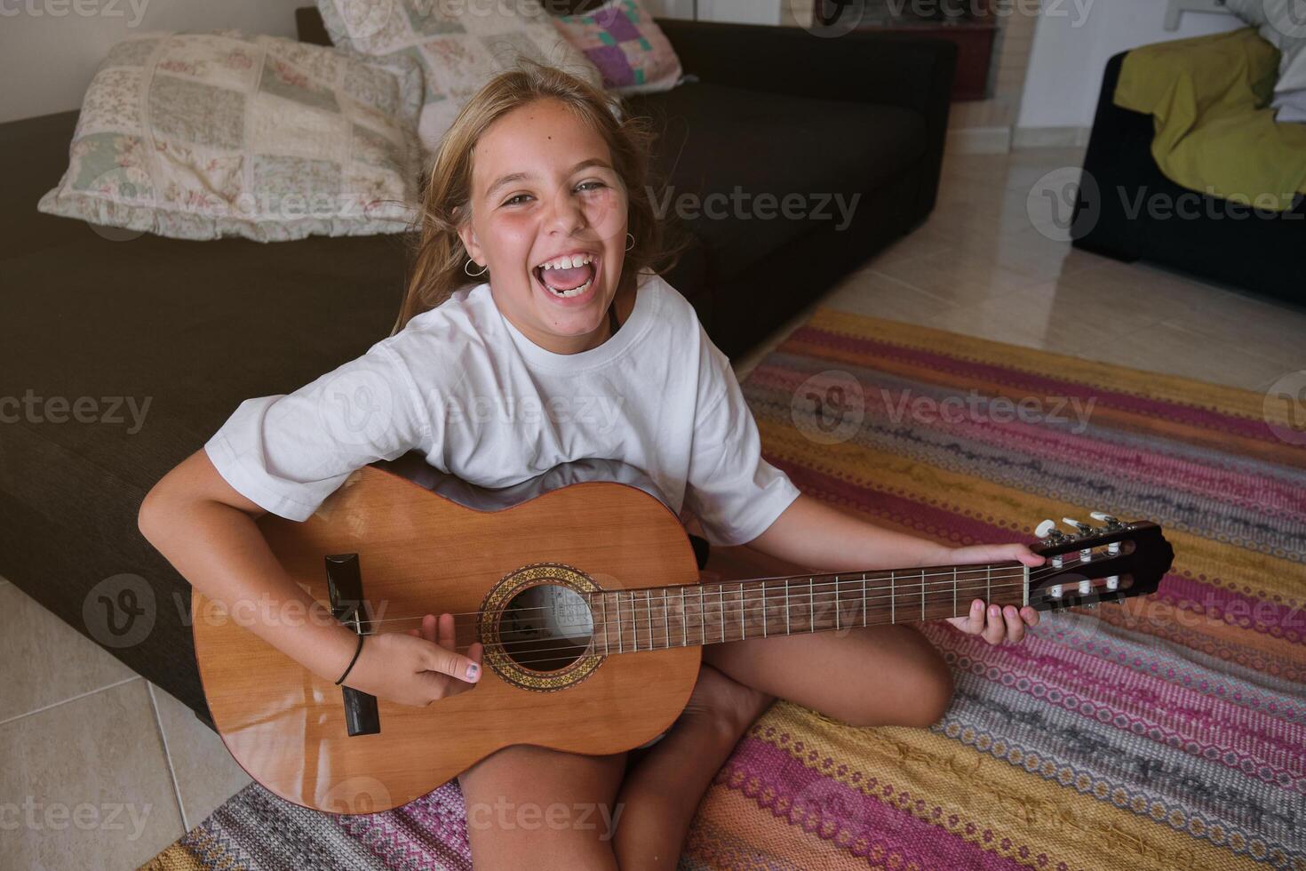 Girl sitting on the floor of a house playing a guitar and singing photo