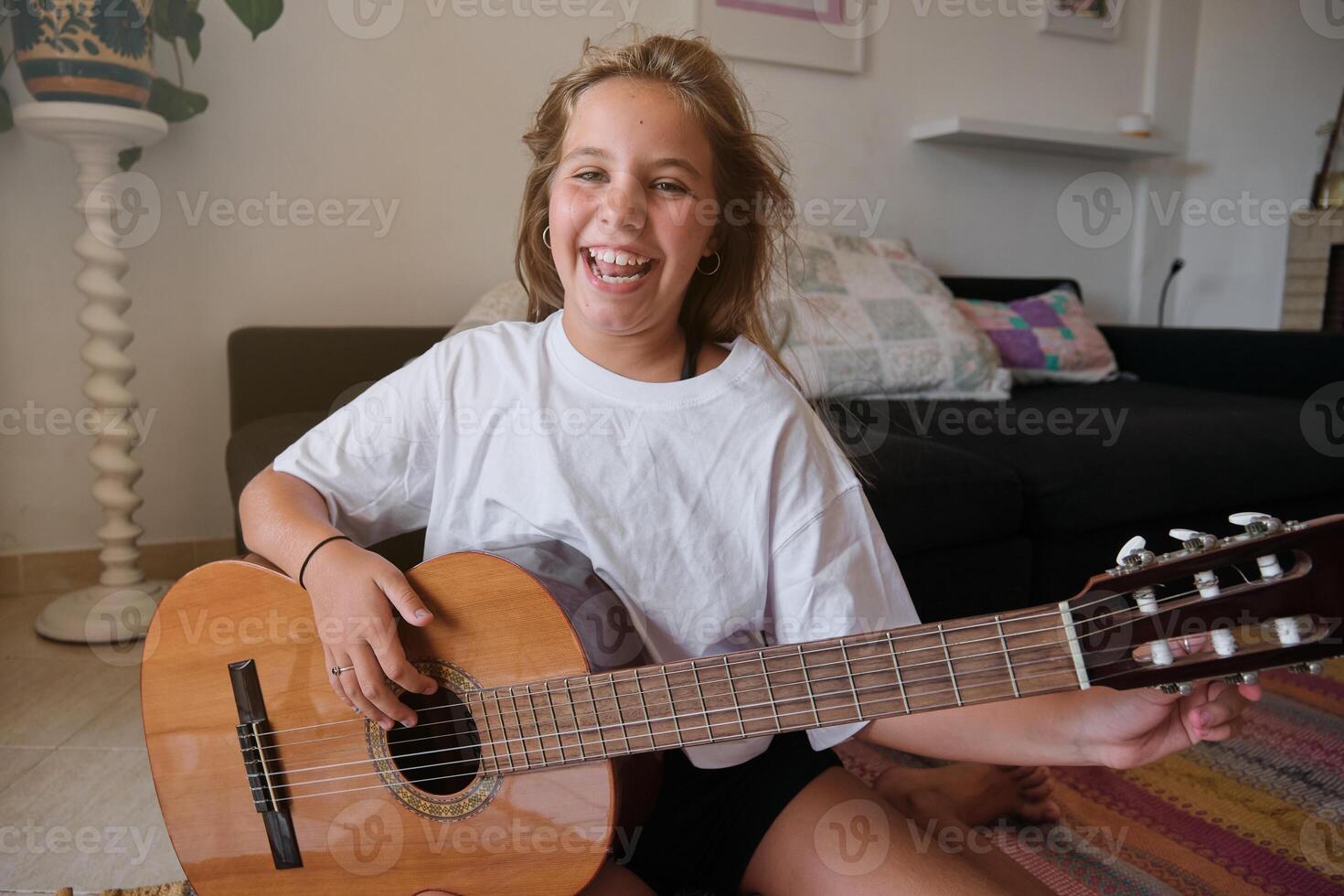 Smiling girl looking at camera while tuning a guitar in a house photo