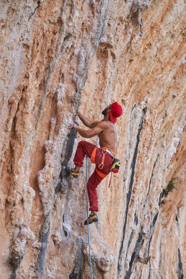 Muscular man climbing rocky cliff photo