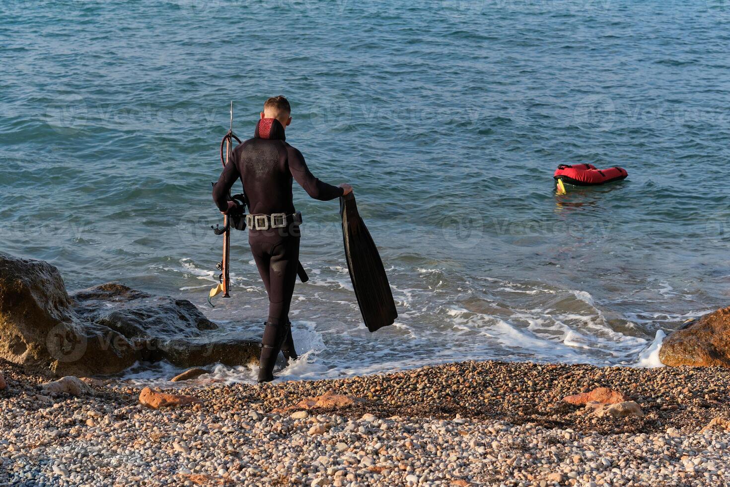 Anonymous man in wetsuit walking in seawater with flippers and speargun photo