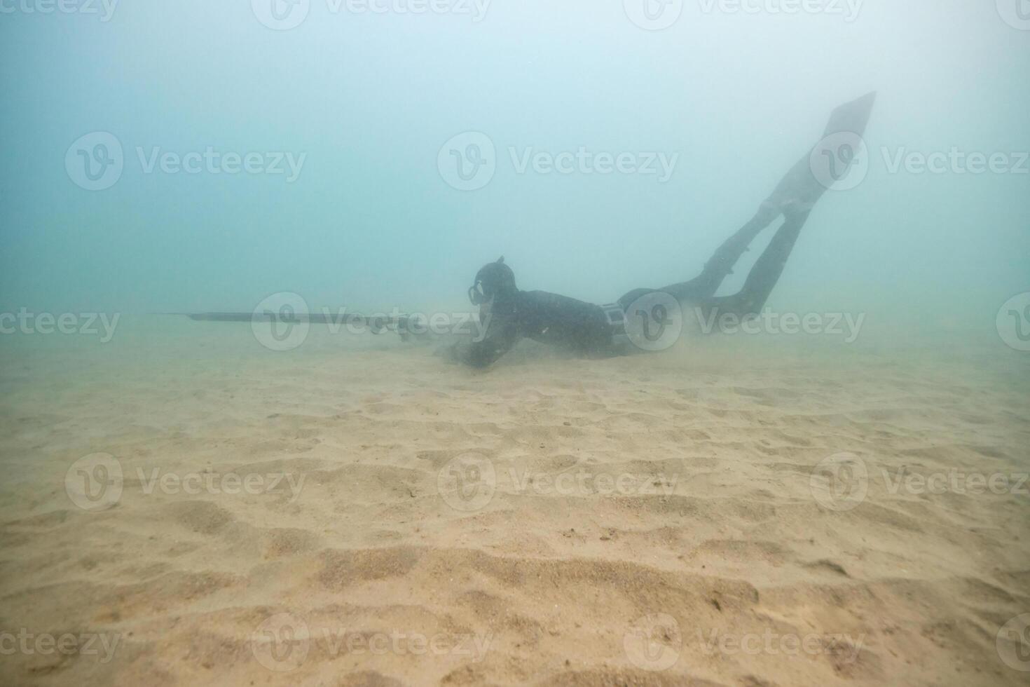 Underwater anonymous fisherman hunting near sandy bottom photo