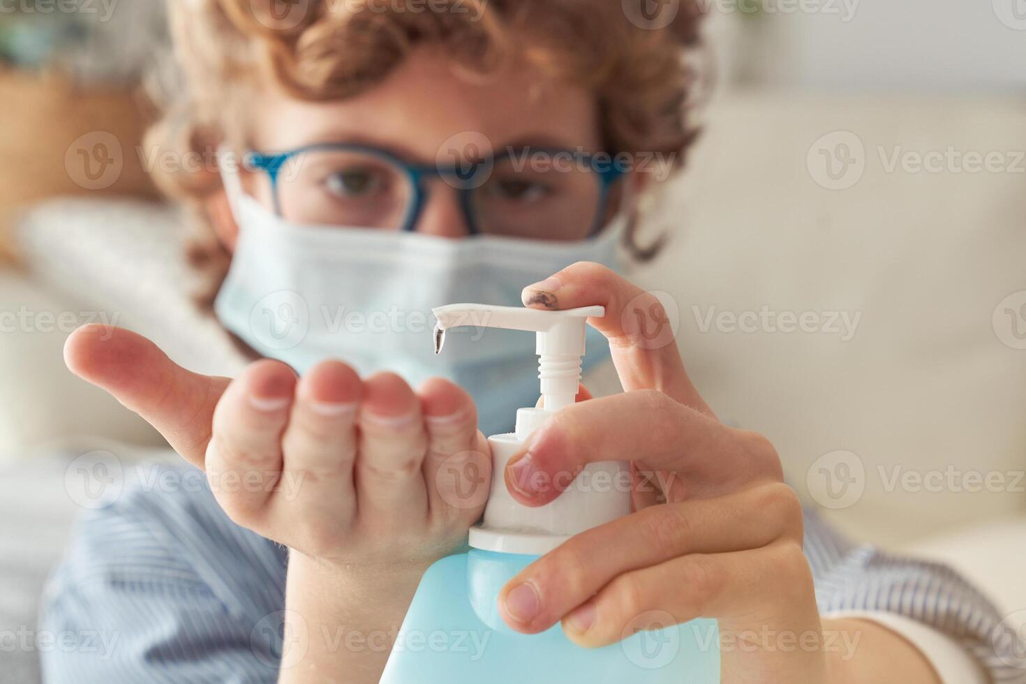 Crop boy in mask applying sanitizer on hand photo