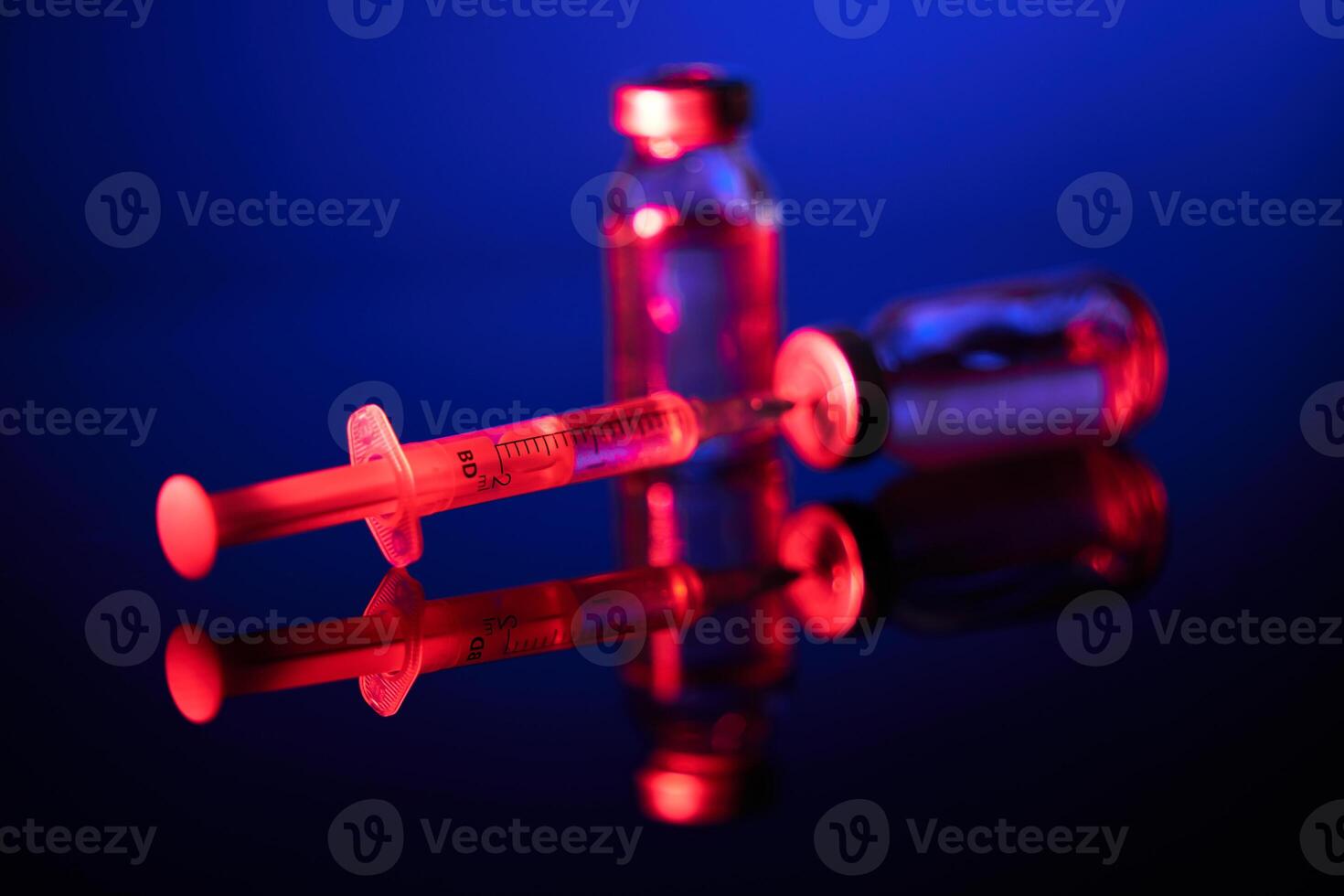 Syringe with needle inserted into vial in dark room photo