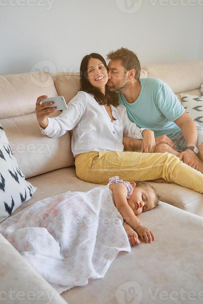 Happy parents taking picture on cellphone near kid at home photo