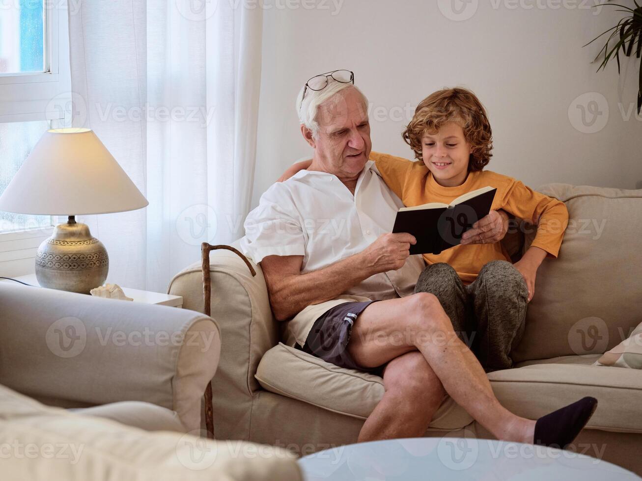 Kid spending time with grandfather while reading book on couch photo