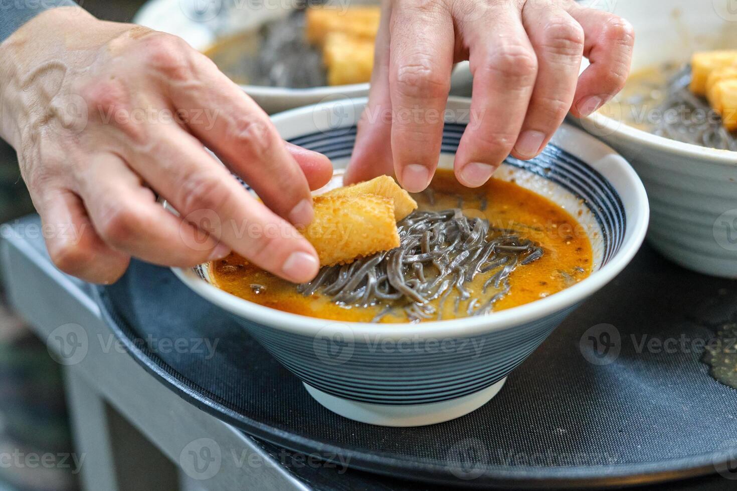 Cook preparing noodle soup with crispy chicken skin photo