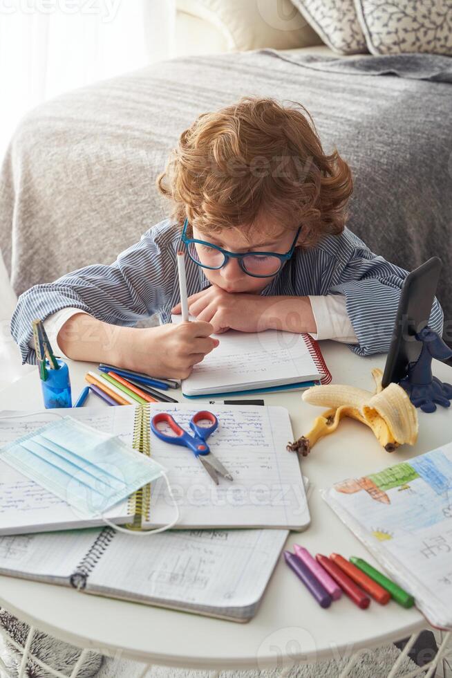 Adorable boy taking notes in notebook at home photo