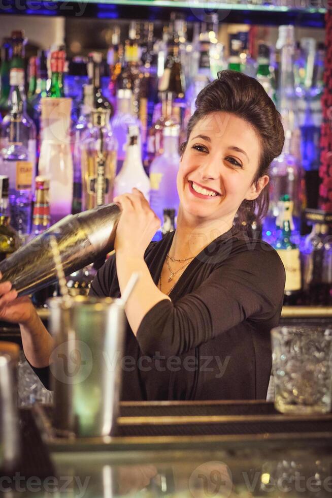 Positive female barkeeper shaking cocktail in bar photo
