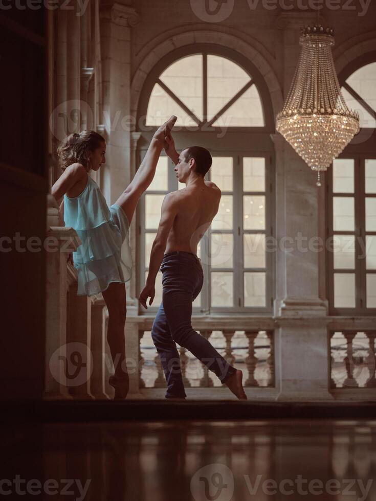 Ballet dancer raising leg of female partner in hall photo