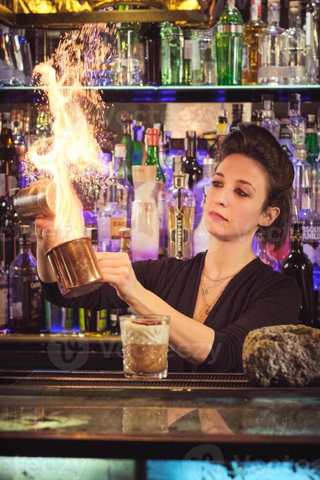 Concentrated female barkeeper making flame while mixing cocktail photo