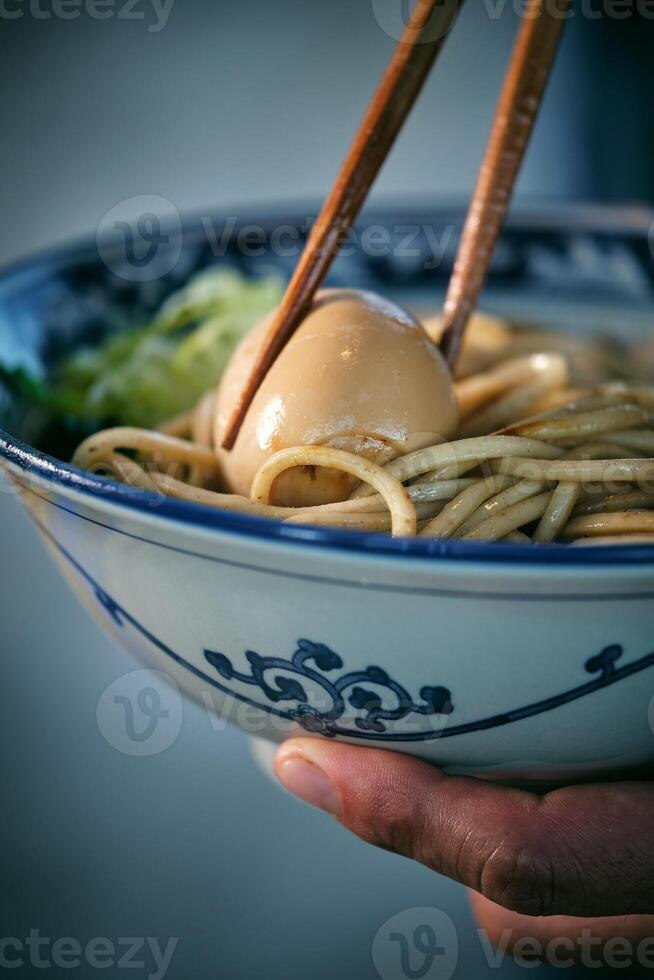 Crop person with boiled egg between chopsticks in ramen photo