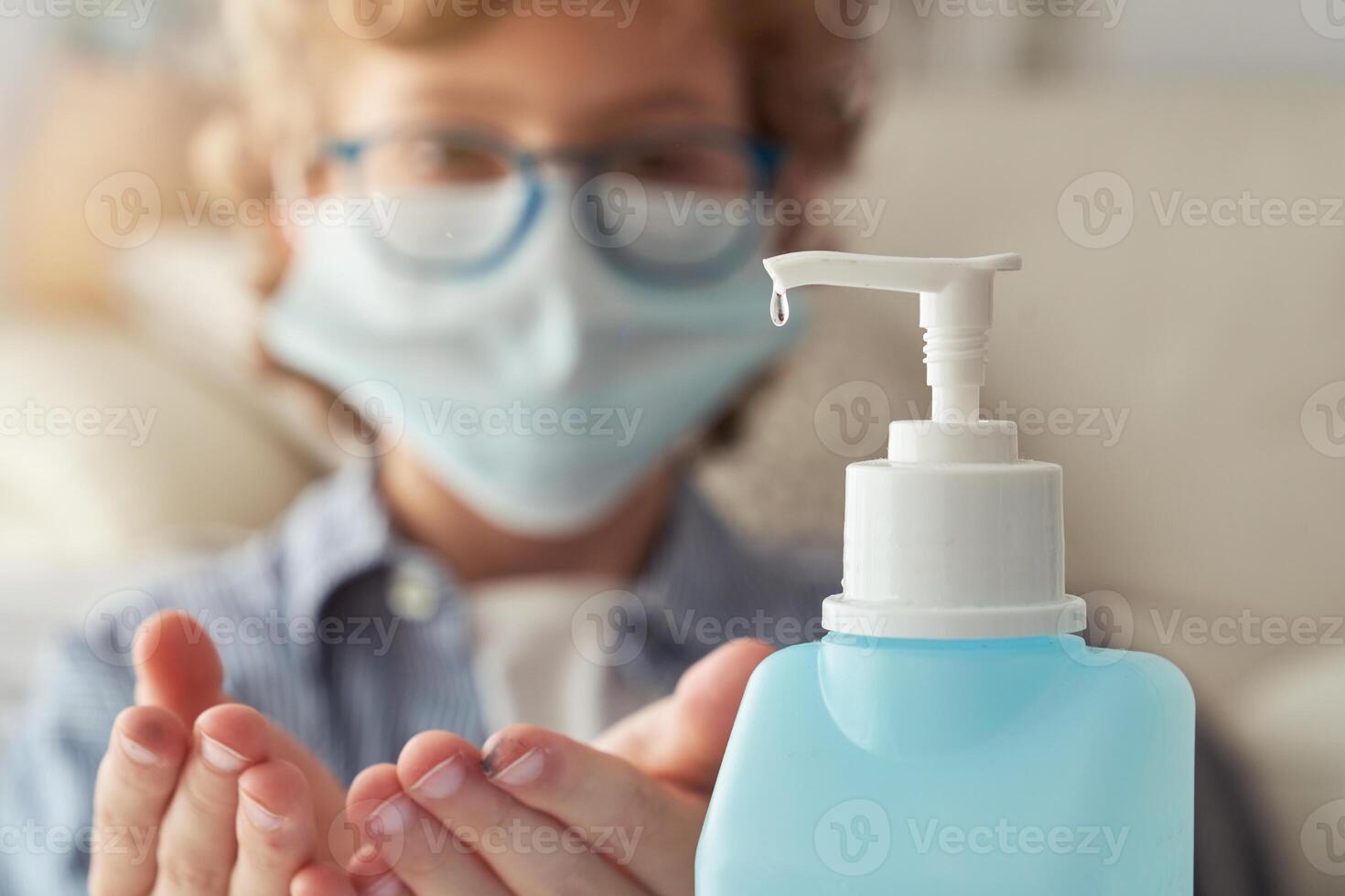 Crop child in mask applying sanitizer on hands photo