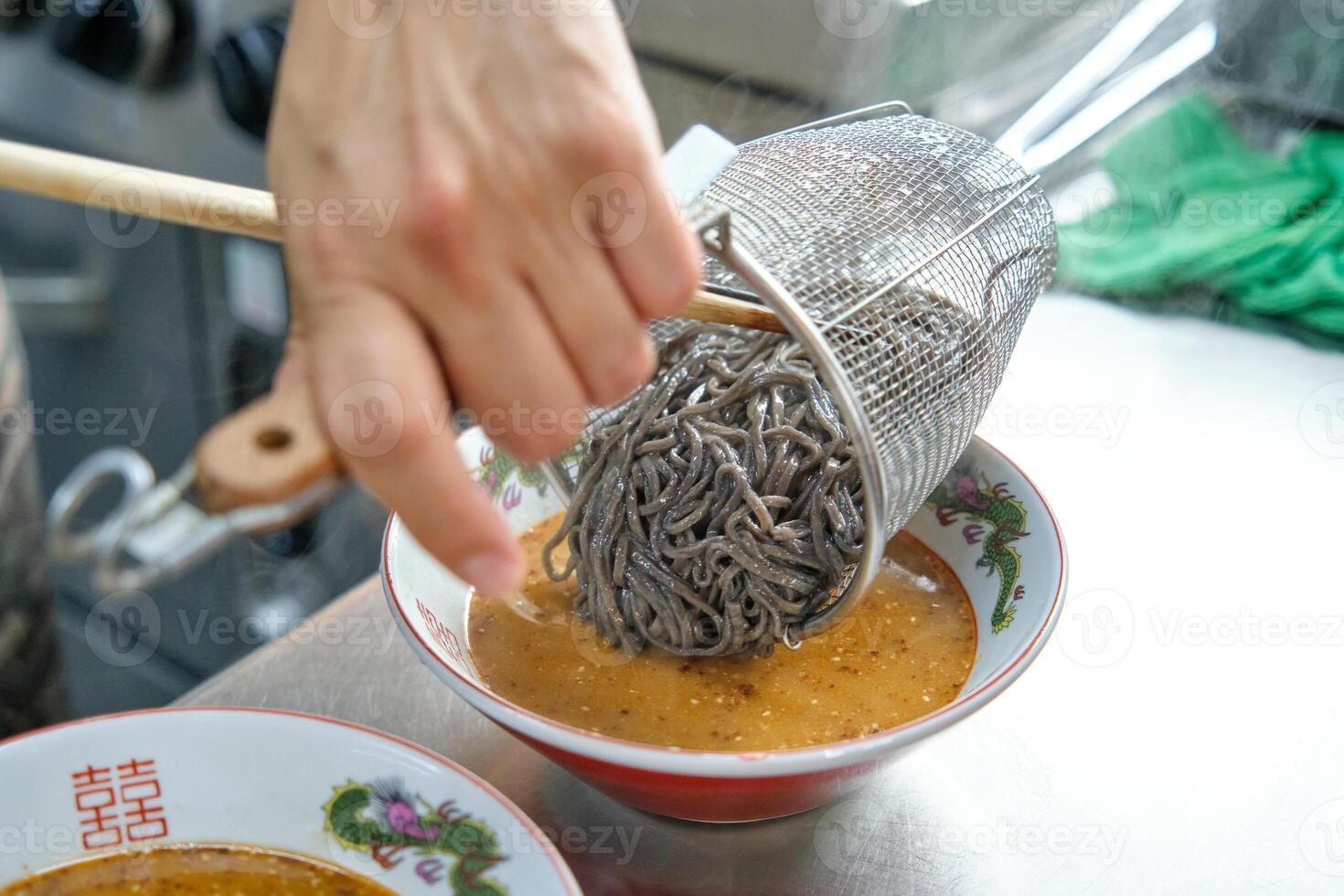 Cook adding boiled noodles to bowl of broth photo