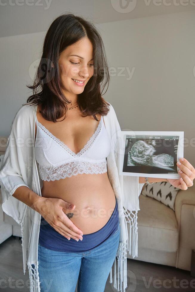 Happy pregnant lady with ultrasound image at home photo