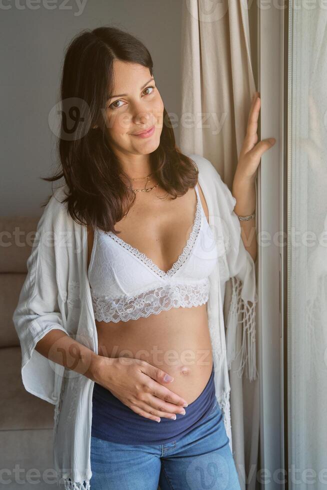 Happy expecting woman touching belly and looking at camera photo