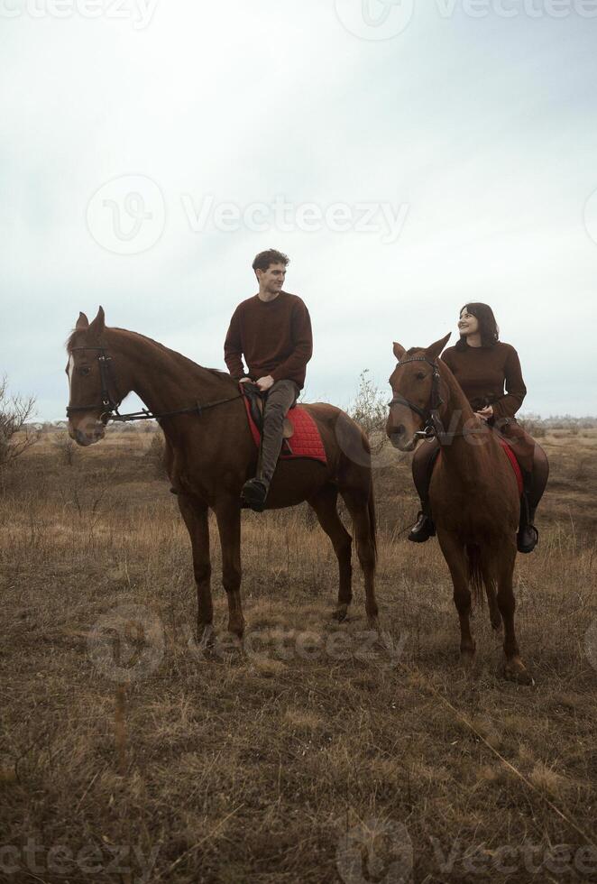 Young romantic couple horse riding, against the background of a field with autumn grass. galloping across the fields, stylishly dressed in brown shades. smiling during a romantic honeymoon. photo