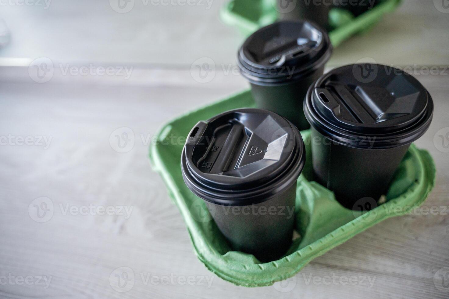 Three black plastic glasses with a drink stand on a light wooden table in the office. The glasses are covered with lids in a stand for transportation. Top view photo
