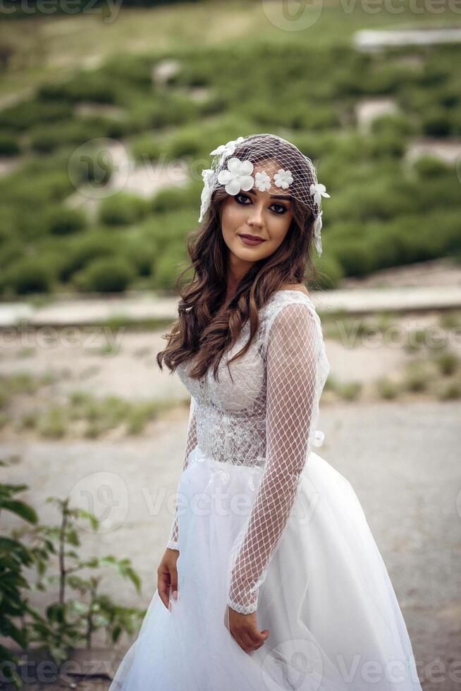 young girl bride in a white dress in a spring forest on a wedding day, beautiful brunette in a long stylish plan among huge trees. hair veil with flowers in vintage style photo