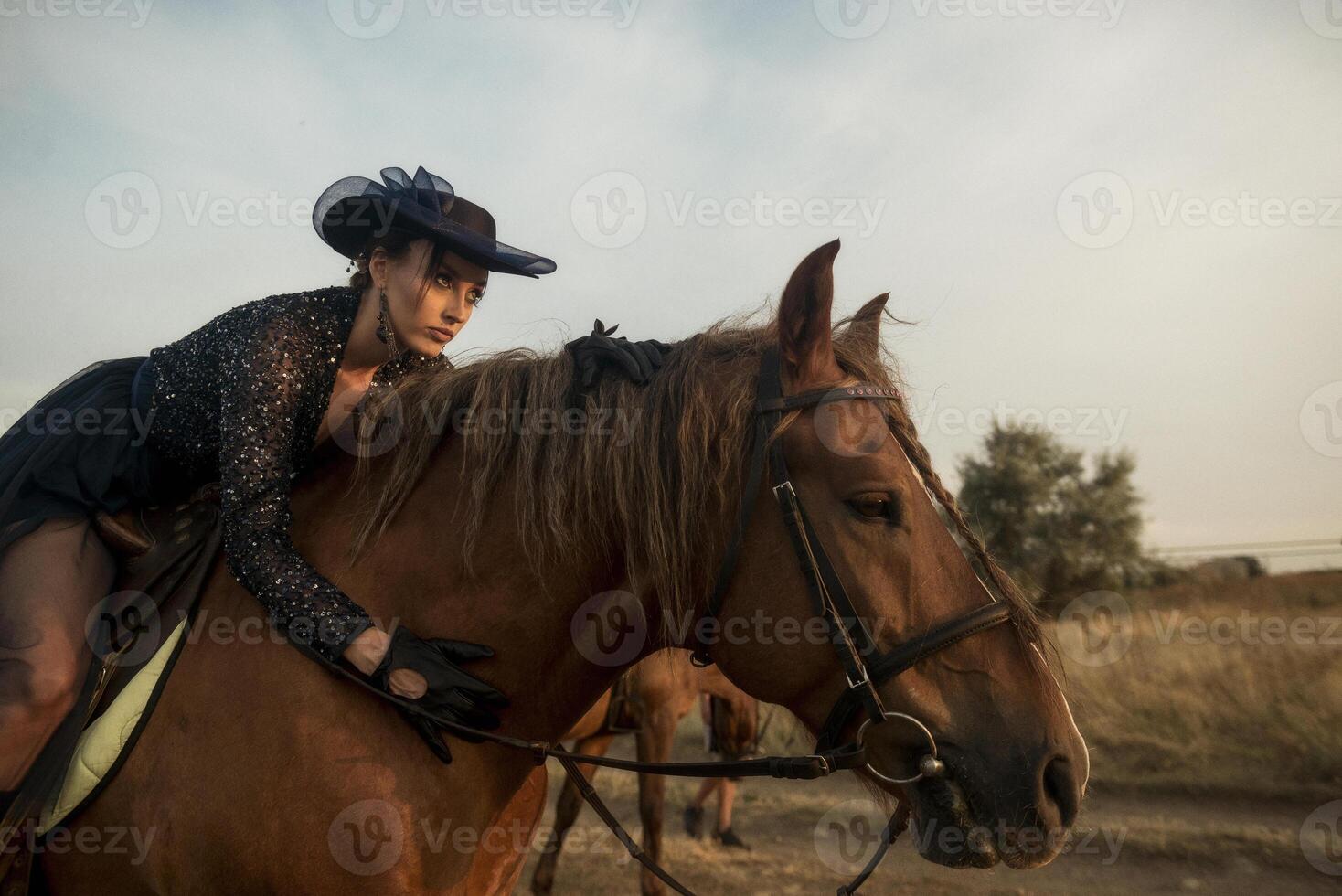 elegant girl in long dress, gloves and hat upside down on horse, in the middle of field. girl has refined and vintage style. brown horse, in rays of setting sun. horizontal photo
