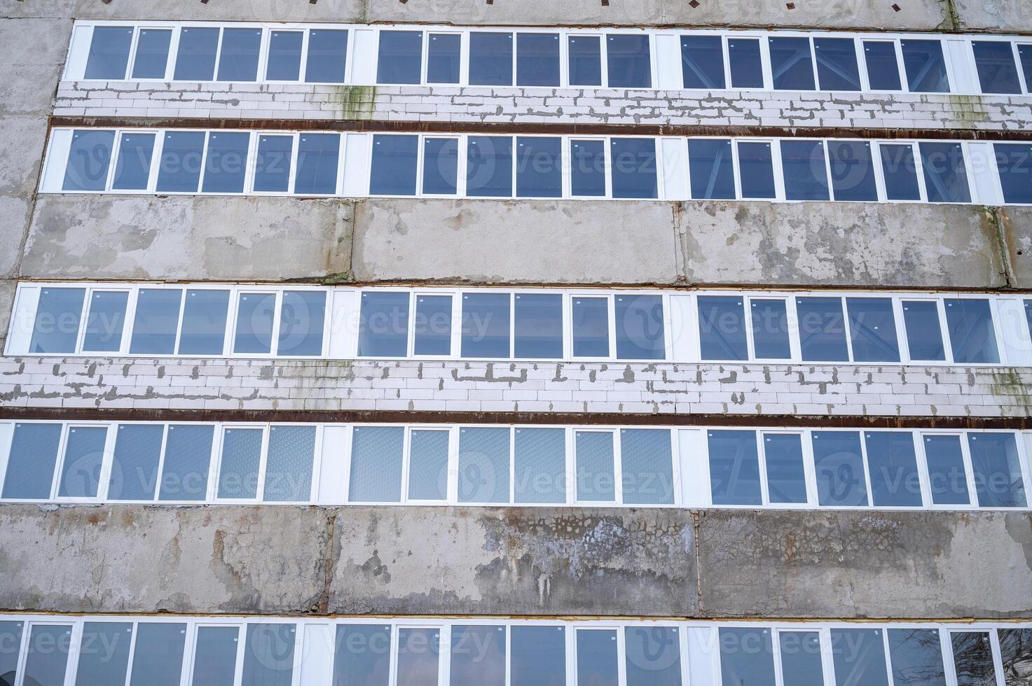 The facade of an industrial building made of white brick and concrete slabs. The building has many white plastic windows. A sign on the side of a building. High quality photo. photo