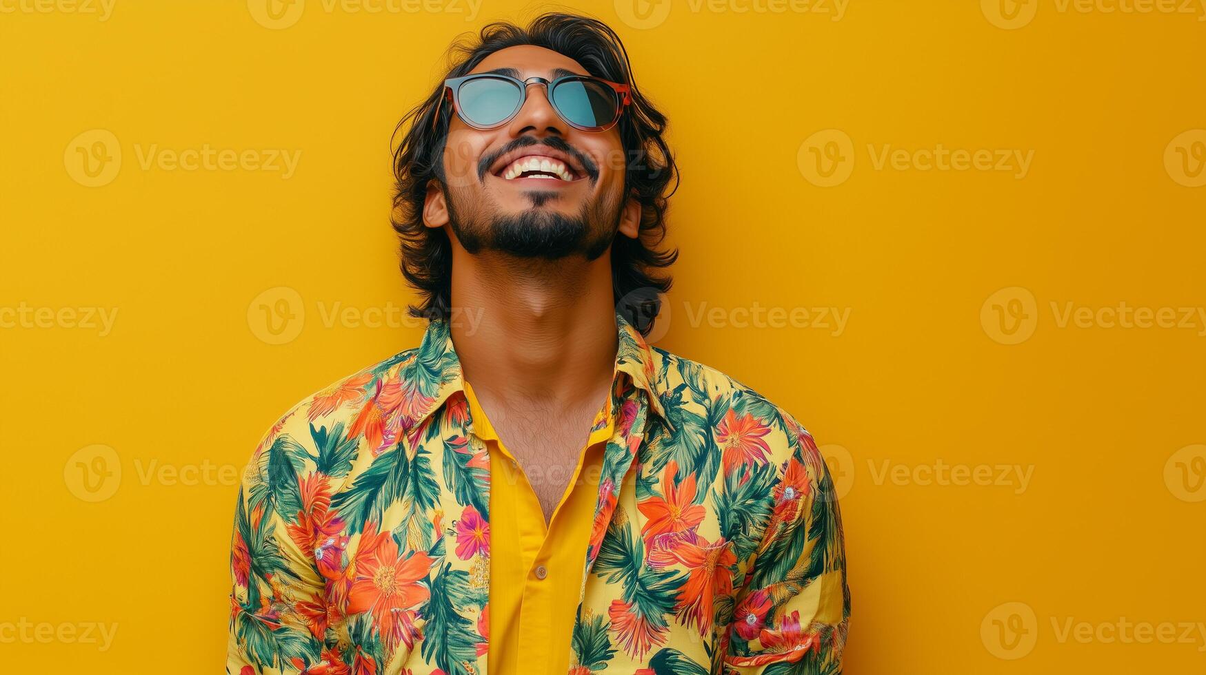 A man wearing a yellow shirt with flowers on it is smiling. He is wearing sunglasses and has a beard photo