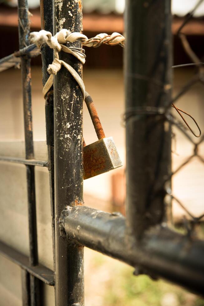 Rusty padlock tied to black metal gate highlights security concerns. photo