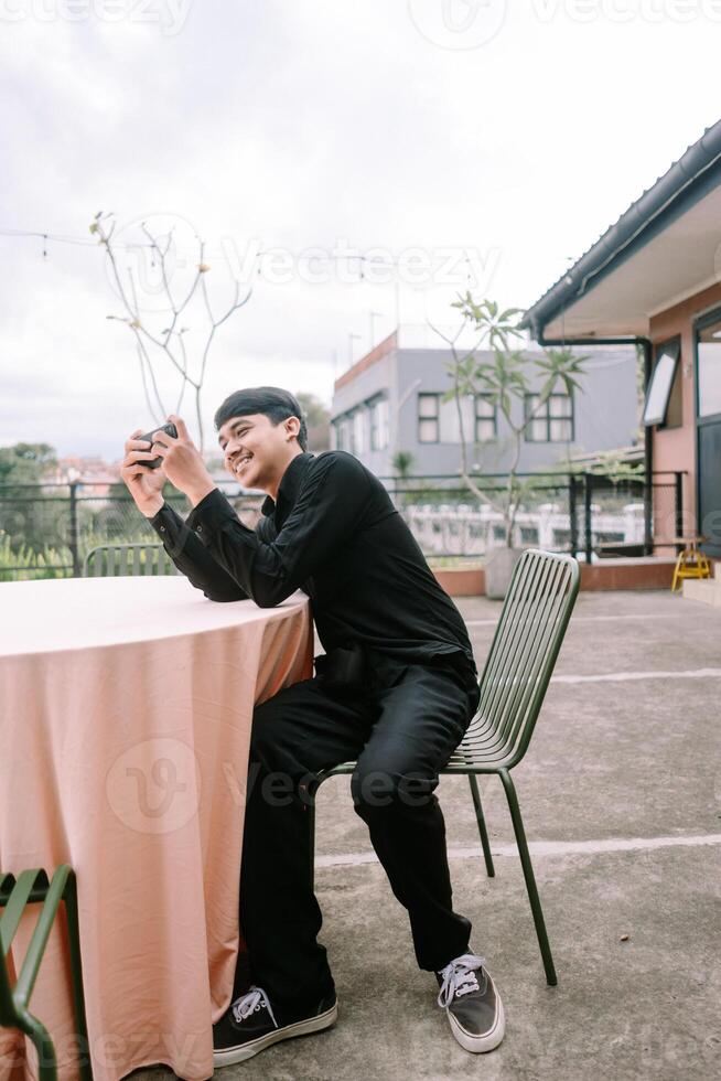 Young man smiling and using a camera while sitting at outdoor cafe photo