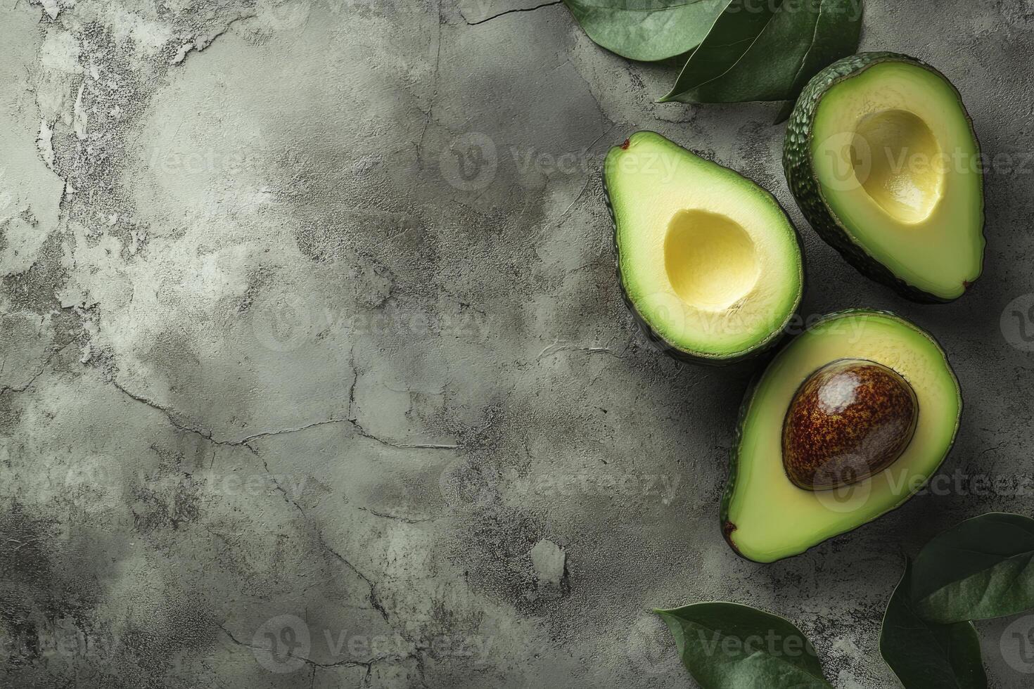Sliced Avocado Halves with Leaves on Gray Textured Background Close Up photo