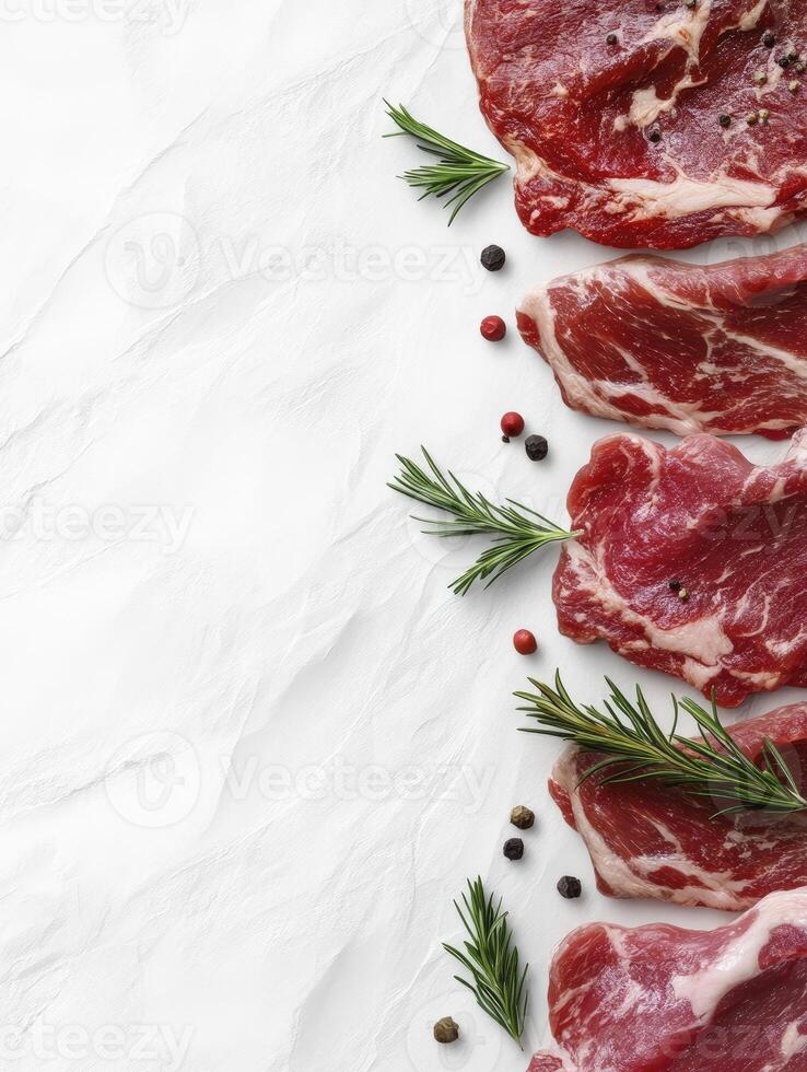 Arrangement of Raw Steaks with Rosemary and Pepper on White Background photo