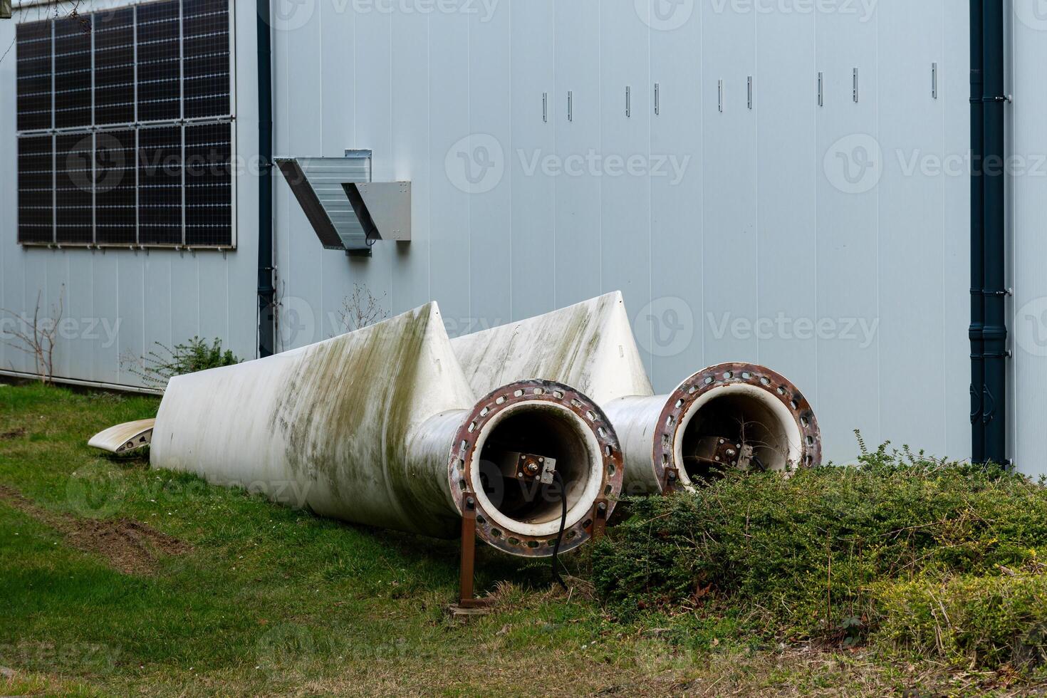 Two large, discarded wind turbine blades are resting against a photo