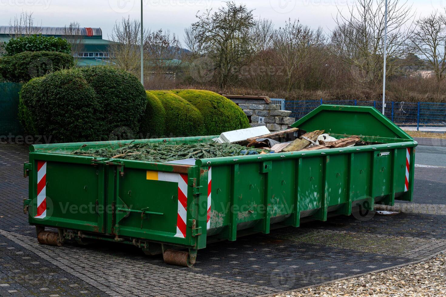 A green dumpster is located in an urban setting, filled with various photo