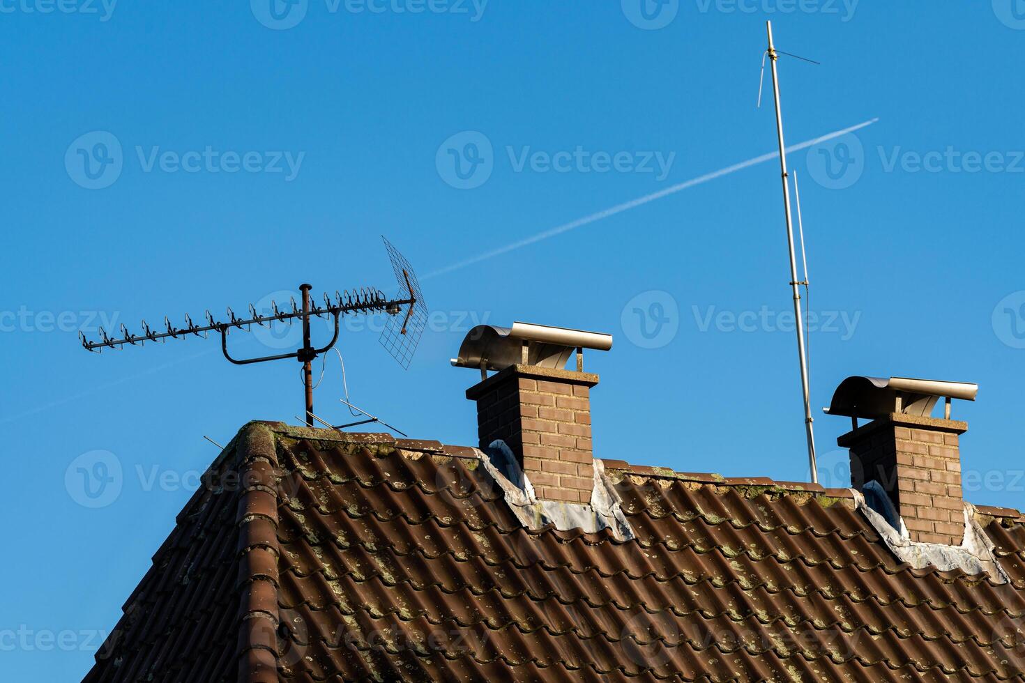 Two chimneys and an antenna stand on a sloped roof against a vibrant photo