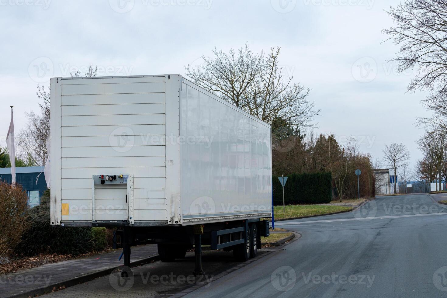A white cargo trailer stands alone on a roadside in a largely empty photo