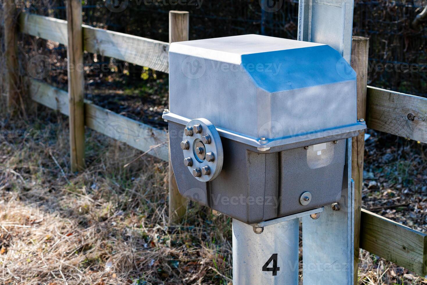 A metal control box is securely placed on a post beside a wooden fence photo