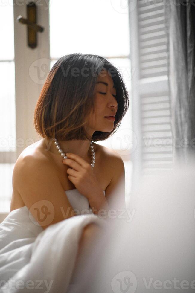 She leans into the window frame, lost in thought, the pearls reflecting the light with a subtle grace. photo