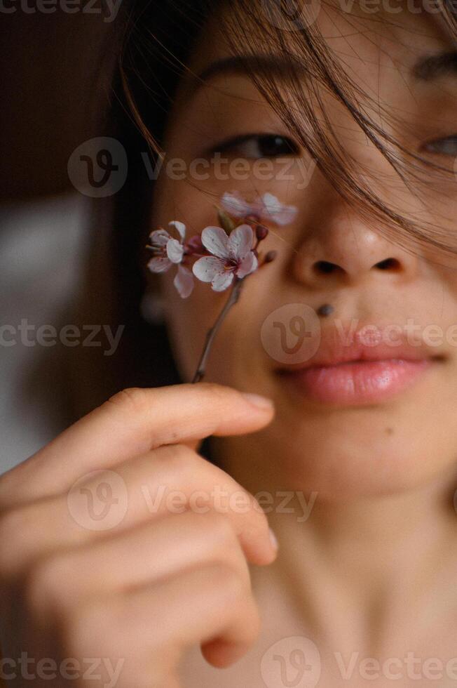 A beautiful Asian woman holds a branch of delicate pink flowers close to her face. photo