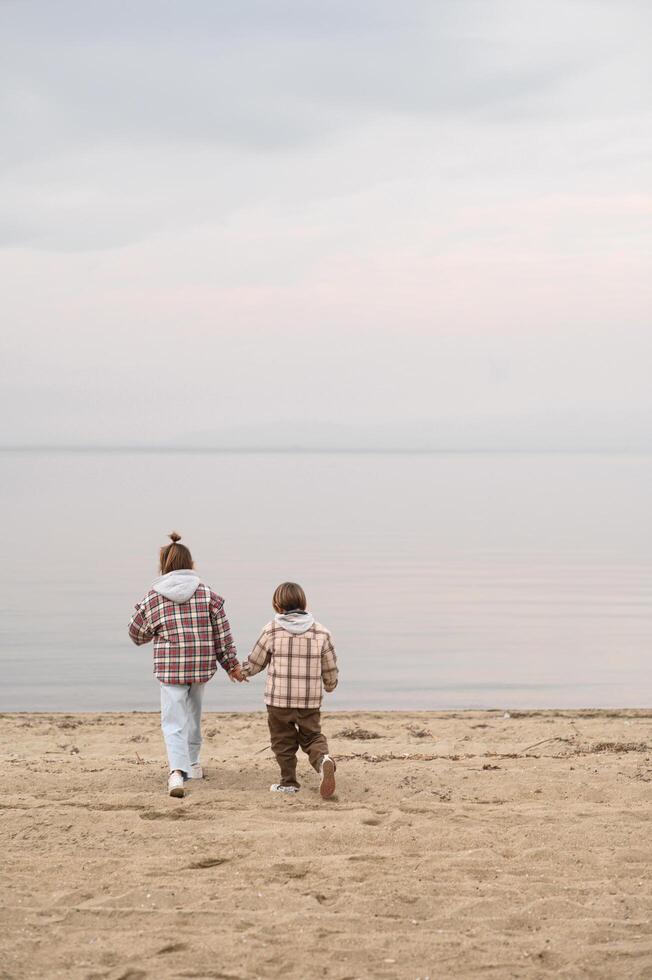 The children dash across the beach, their checkered coats fluttering as they play near the waters edge photo