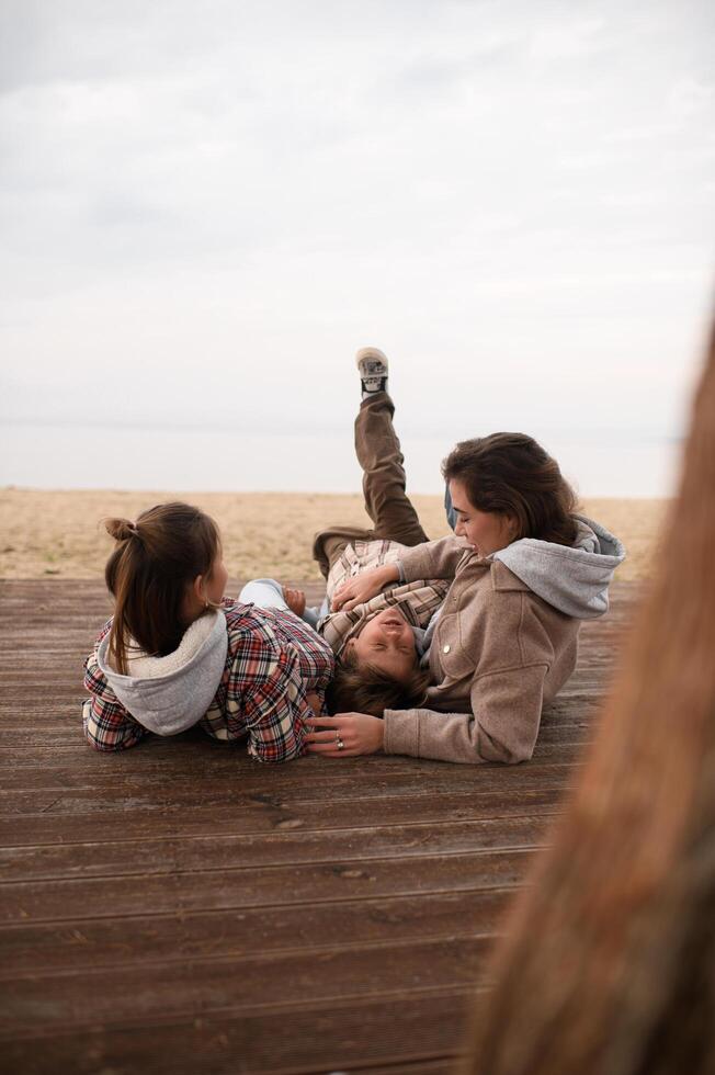 A tender moment as a mother and her children hug each other on a wooden pier, with waves gently rolling in the background photo