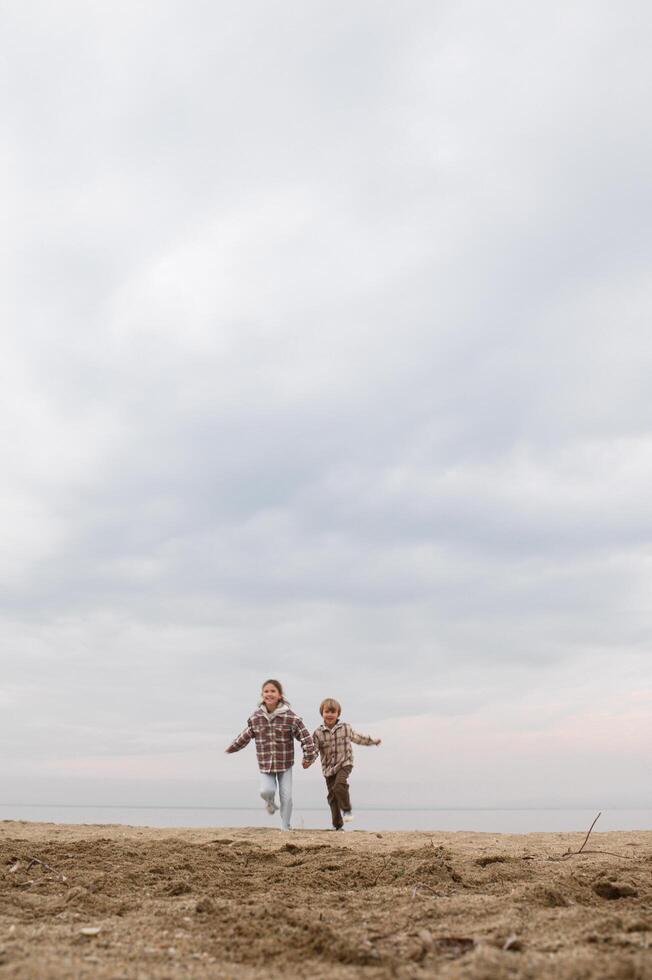 Waves crash as two kids in flannel shirts chase each other. photo