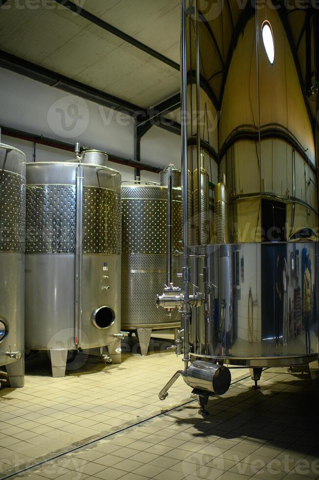 Industrial stainless steel vats filled with fermenting wine inside a high-tech winery photo