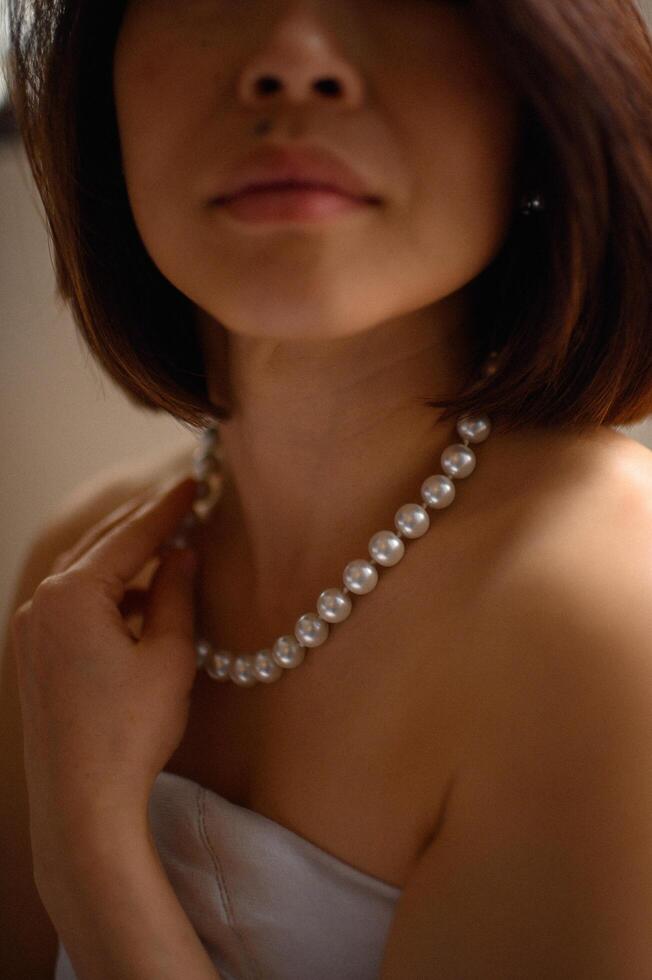 A close-up of a brunette with a sleek bob touching a pearl necklace on her chest. photo
