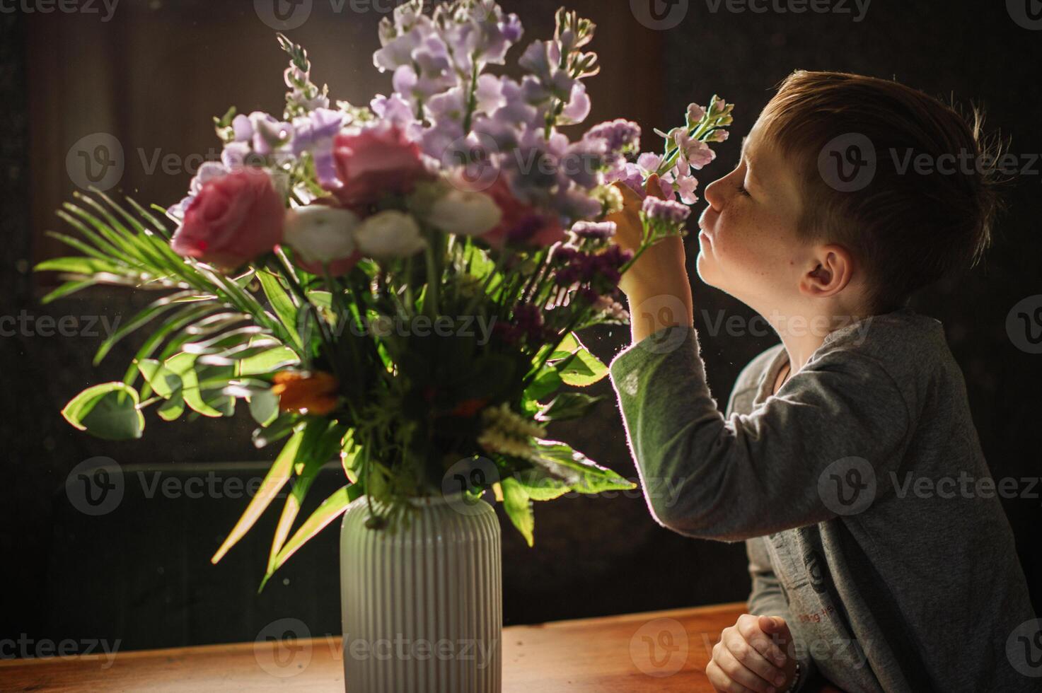 A curious child leans over the table, his nose almost touching the fragrant blossoms. photo