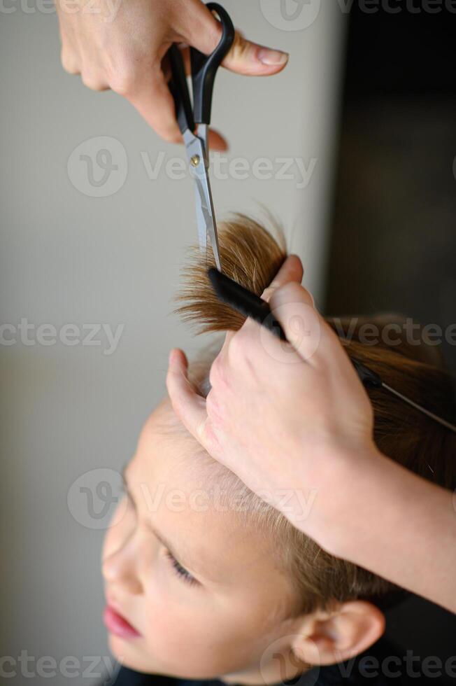A childrens hairstylist carefully trims a boys bangs. photo