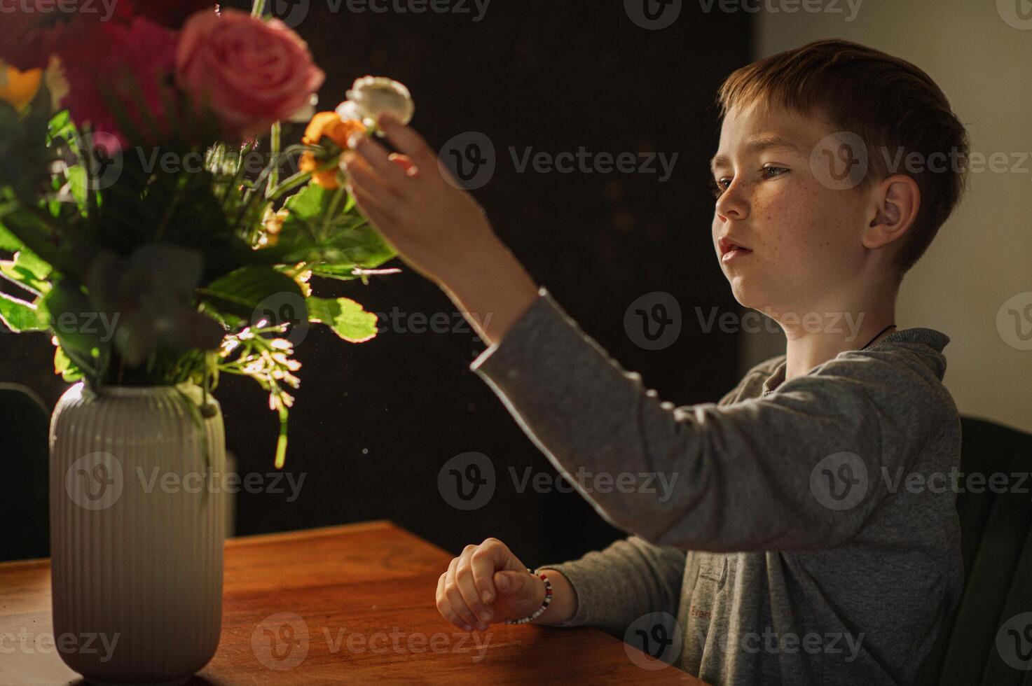Sitting at the table, a boy gently explores a bouquet, lost in its fragrance. photo